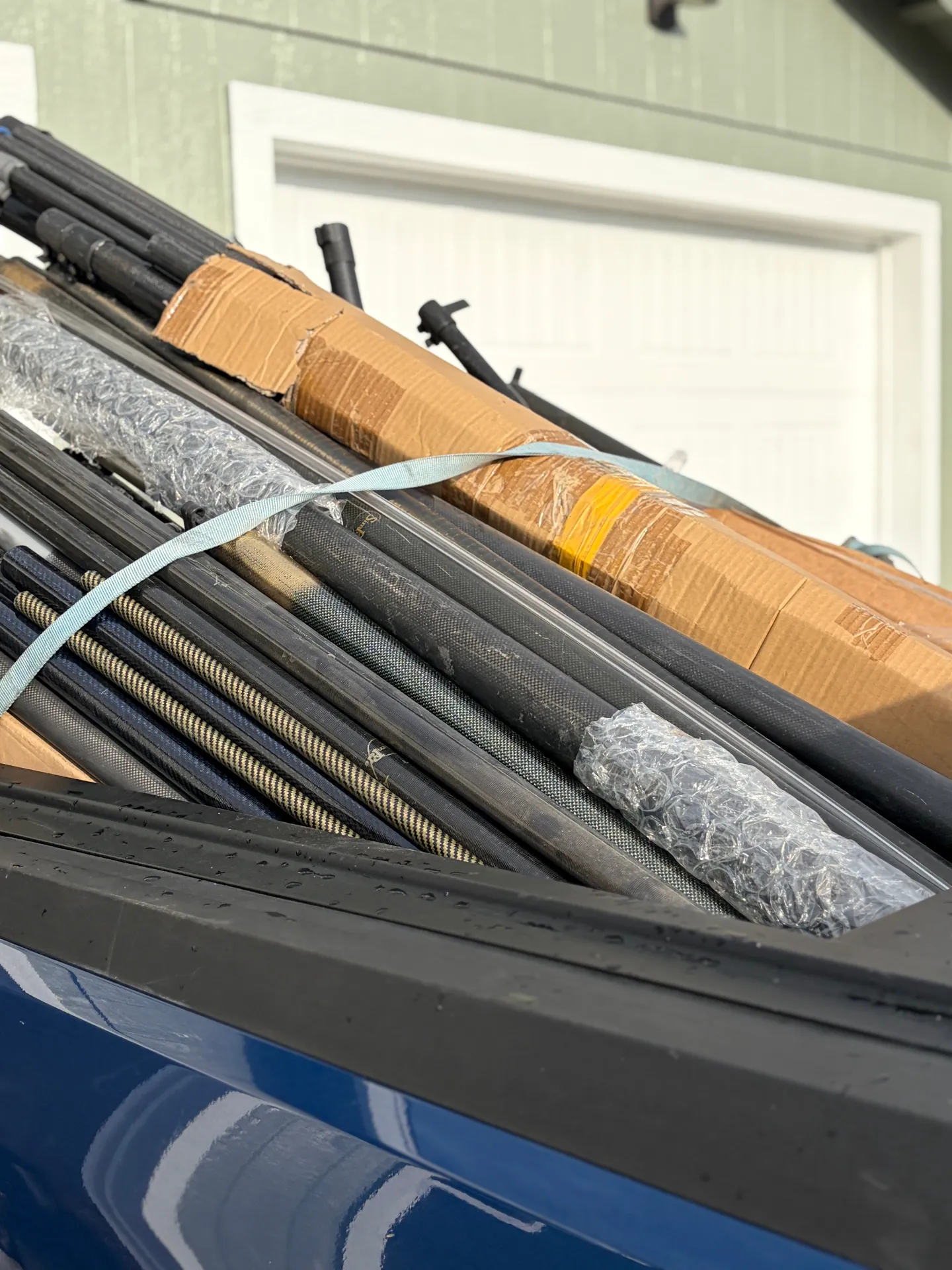 Close-up of bundled carbon fiber water fed pole sections with visible weave, secured with a strap in a truck bed